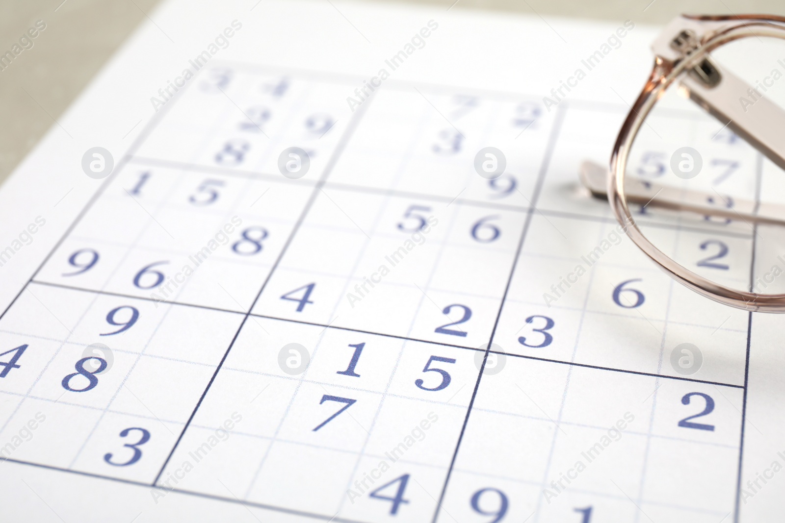 Photo of Sudoku and eyeglasses on table, closeup view