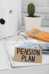 Card with phrase Pension Plan, notebook and money on white office table
