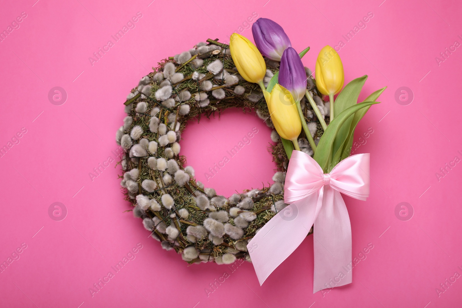 Photo of Wreath made of beautiful willow, colorful tulip flowers and bow on pink background, top view