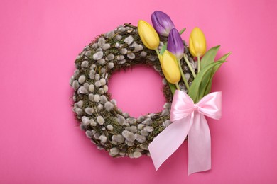 Wreath made of beautiful willow, colorful tulip flowers and bow on pink background, top view