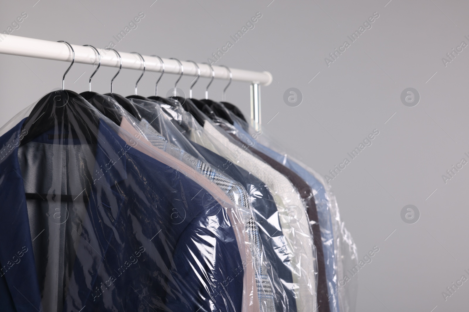 Photo of Dry-cleaning service. Many different clothes in plastic bags hanging on rack against grey background, space for text