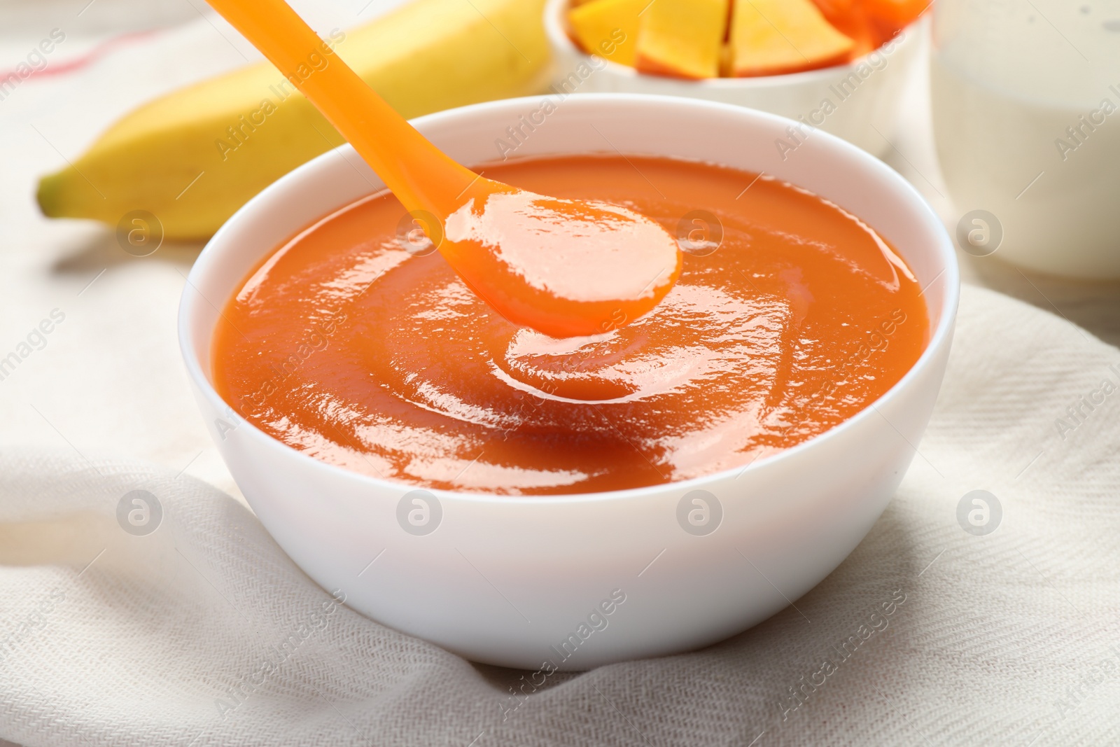 Photo of Spoon of healthy baby food over bowl on table, closeup