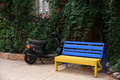 Photo of Beautiful blue and yellow wooden bench near scooter outdoors