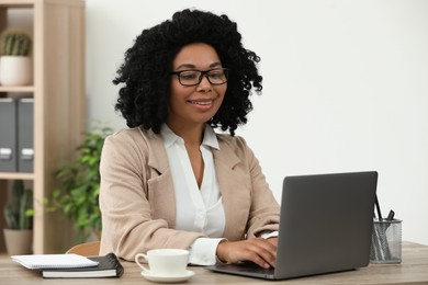 Photo of Happy young woman using laptop at wooden desk indoors