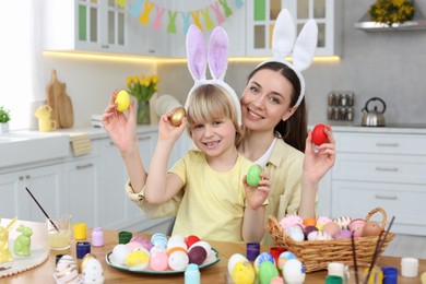 Photo of Mother and her cute son with Easter eggs at table in kitchen