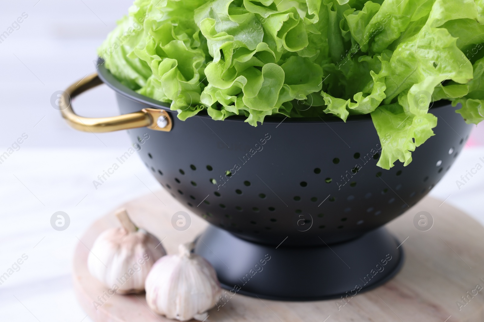 Photo of Fresh lettuce in black colander on white table indoors, closeup