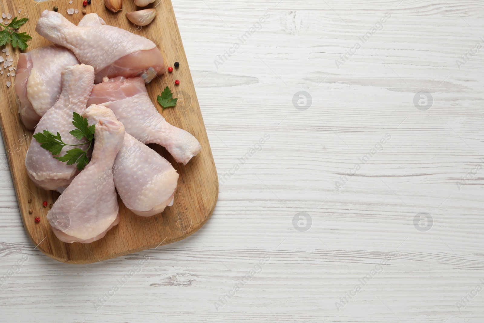Photo of Raw chicken drumsticks with parsley, spices and garlic on white wooden table, top view. Space for text