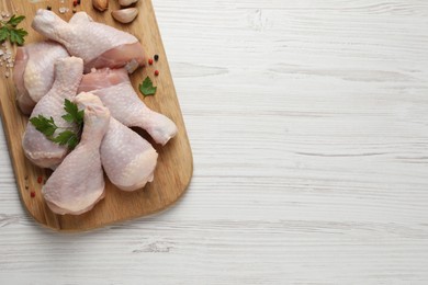 Raw chicken drumsticks with parsley, spices and garlic on white wooden table, top view. Space for text