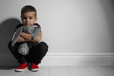 Photo of Sad little boy with toy near white wall, space for text. Domestic violence concept