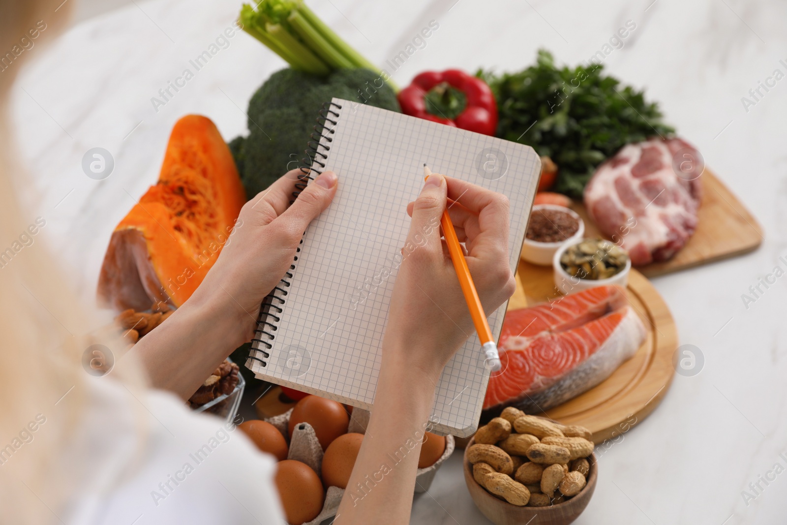 Photo of Woman with notebook and healthy food at white table, closeup. Keto diet