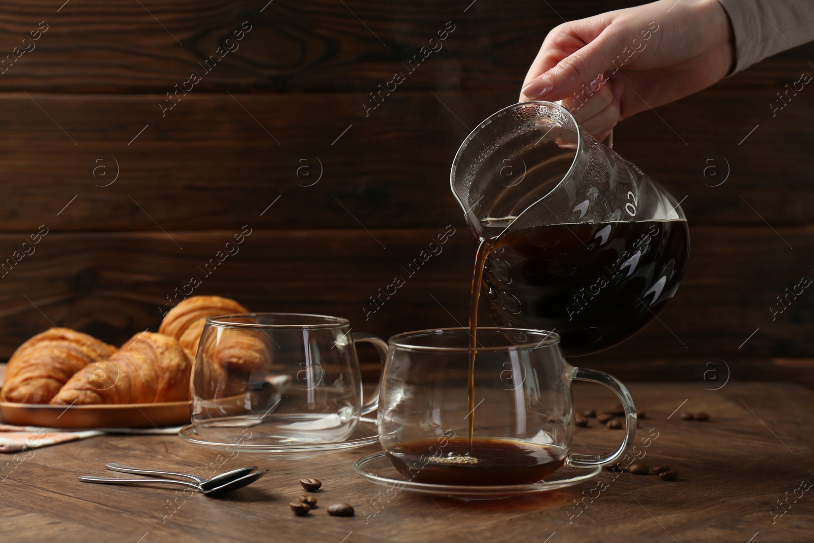 Photo of Woman pouring coffee into glass cup at wooden table, closeup