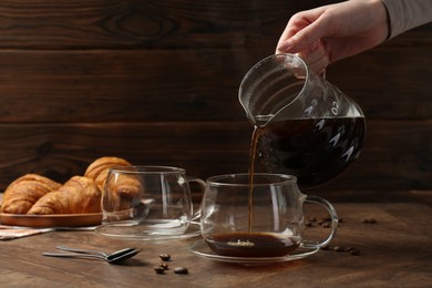 Woman pouring coffee into glass cup at wooden table, closeup