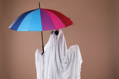 Photo of Person in ghost costume with color umbrella on dark beige background