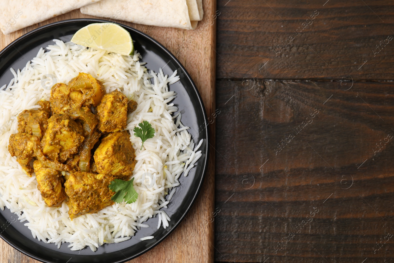 Photo of Delicious chicken curry with rice on wooden table, top view. Space for text