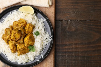 Photo of Delicious chicken curry with rice on wooden table, top view. Space for text