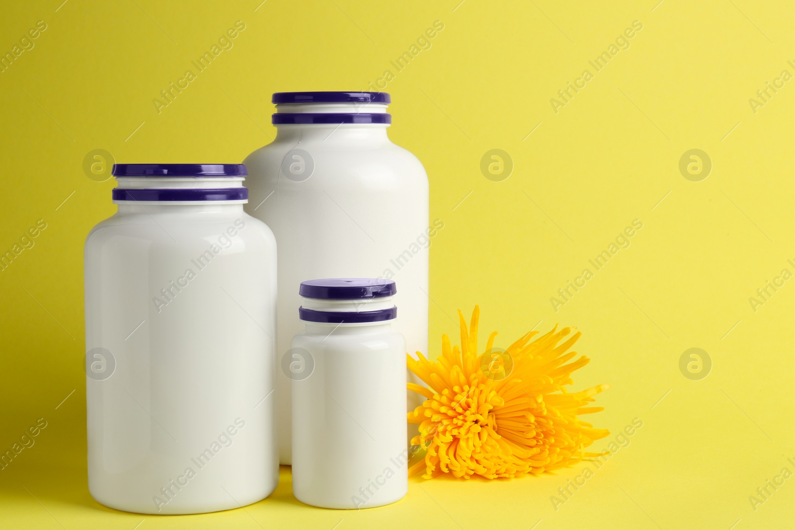 Photo of Medicine bottles near flower on yellow background, space for text