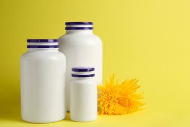 Medicine bottles near flower on yellow background, space for text