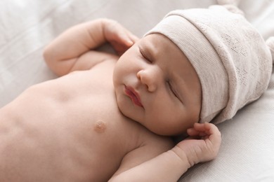 Photo of Adorable little baby with hat sleeping on bed, closeup