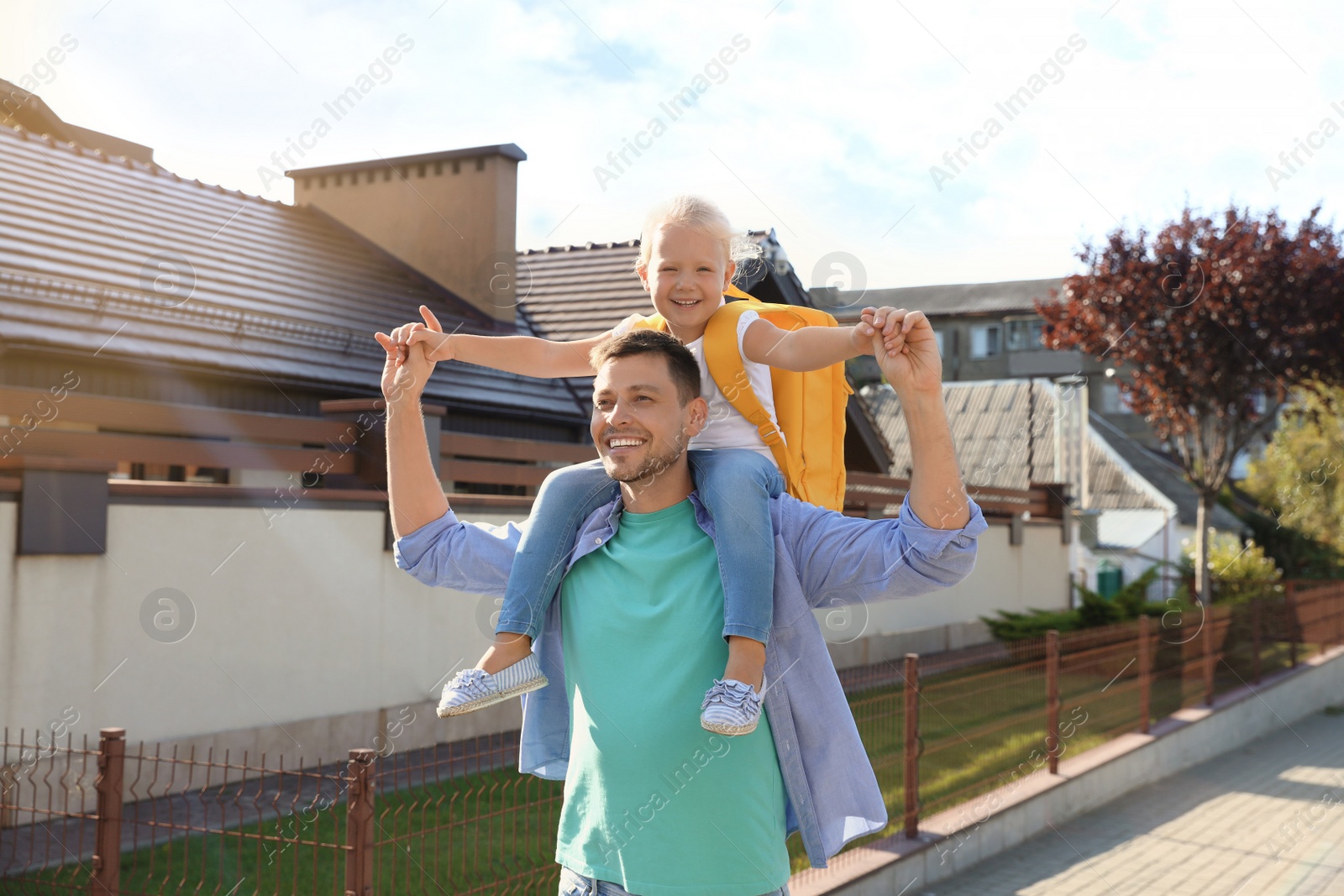 Photo of Happy father carrying his little child with school bag on shoulders outdoors