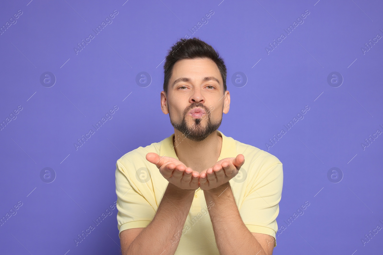 Photo of Handsome man blowing kiss on violet background