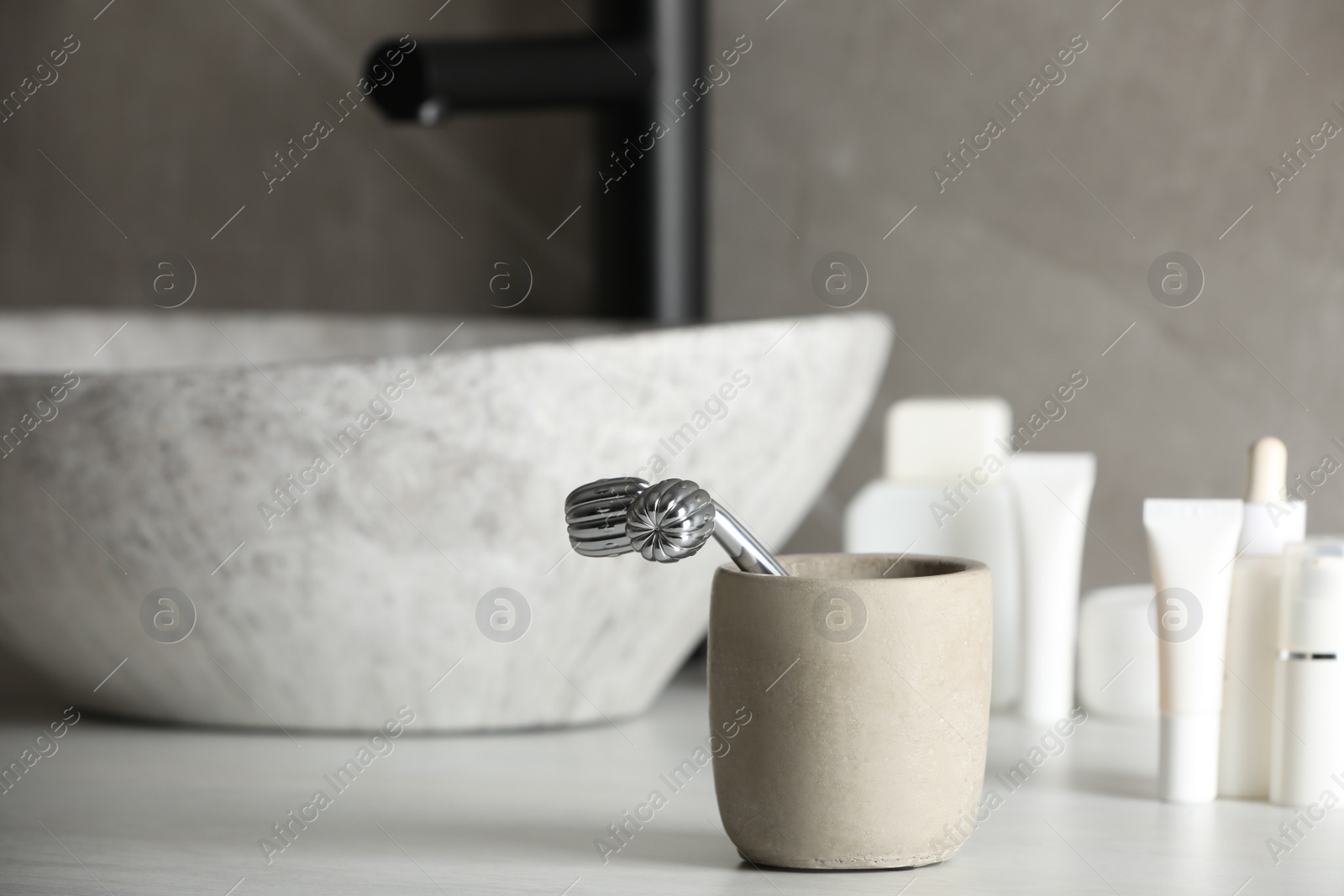 Photo of Holder with metal face roller on counter in bathroom. Space for text