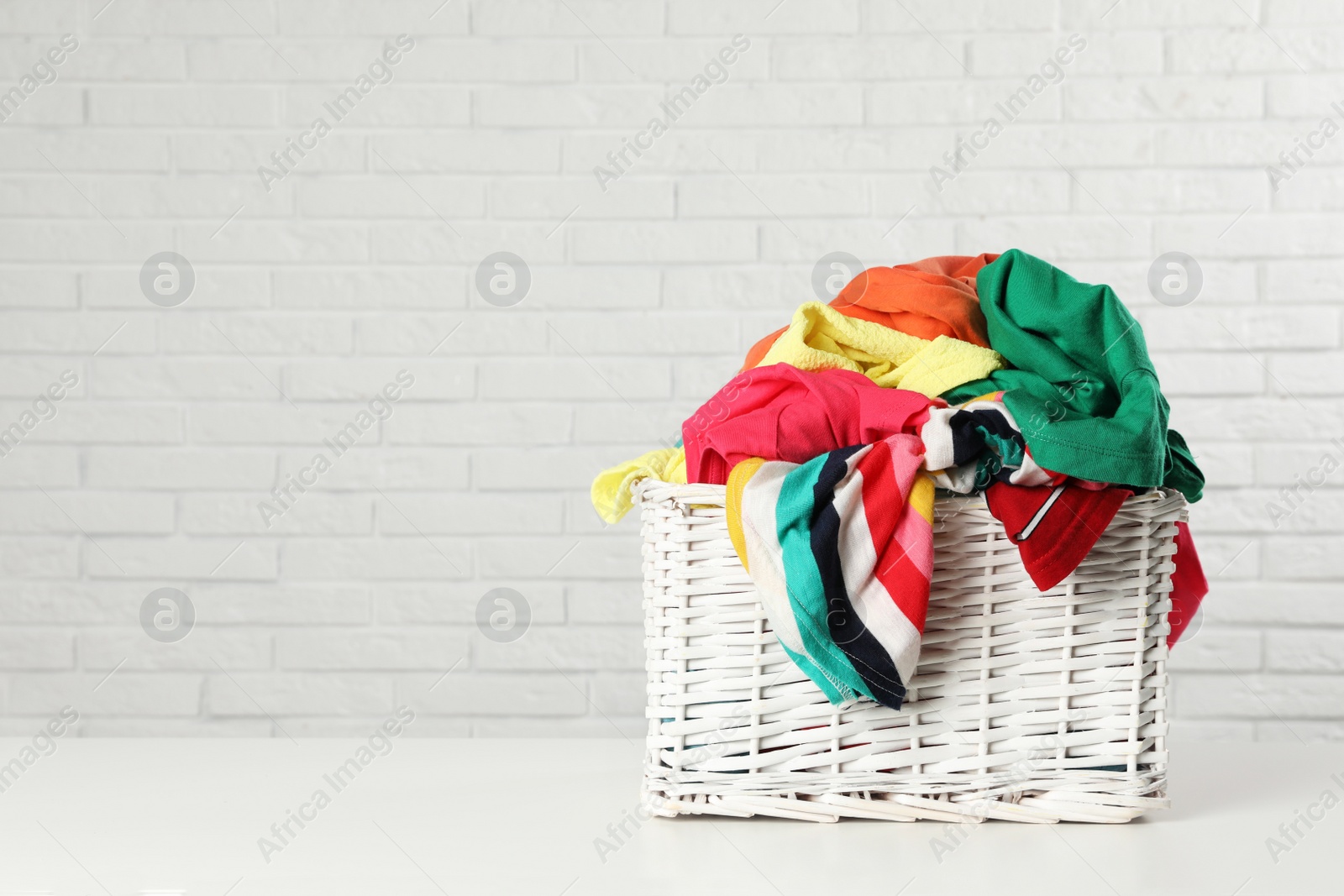 Photo of Wicker basket with laundry on table near white brick wall. Space for text