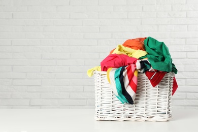 Photo of Wicker basket with laundry on table near white brick wall. Space for text