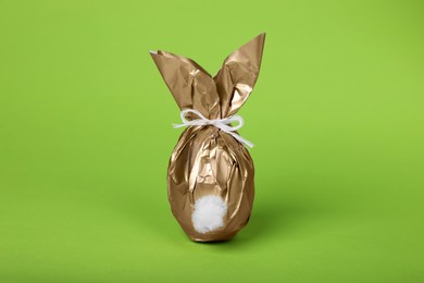 Photo of Easter bunny made of shiny gold paper and egg on green background