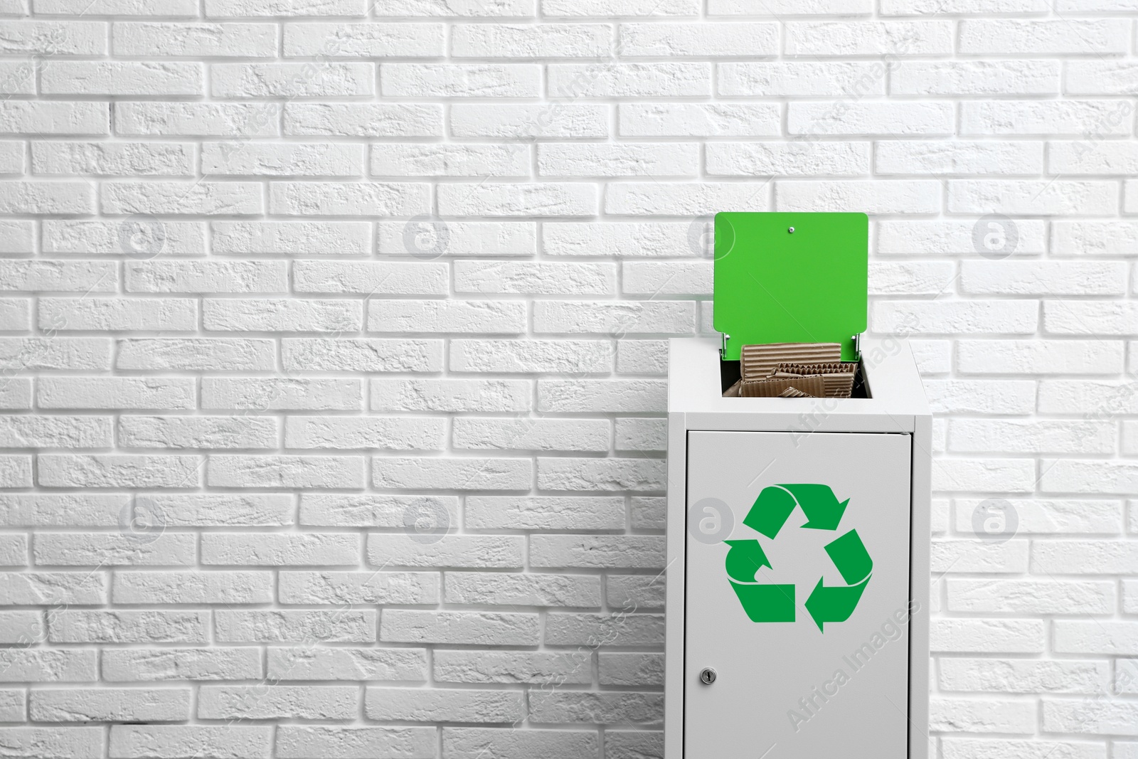 Photo of Overfilled trash bin with recycling symbol near brick wall. Space for text