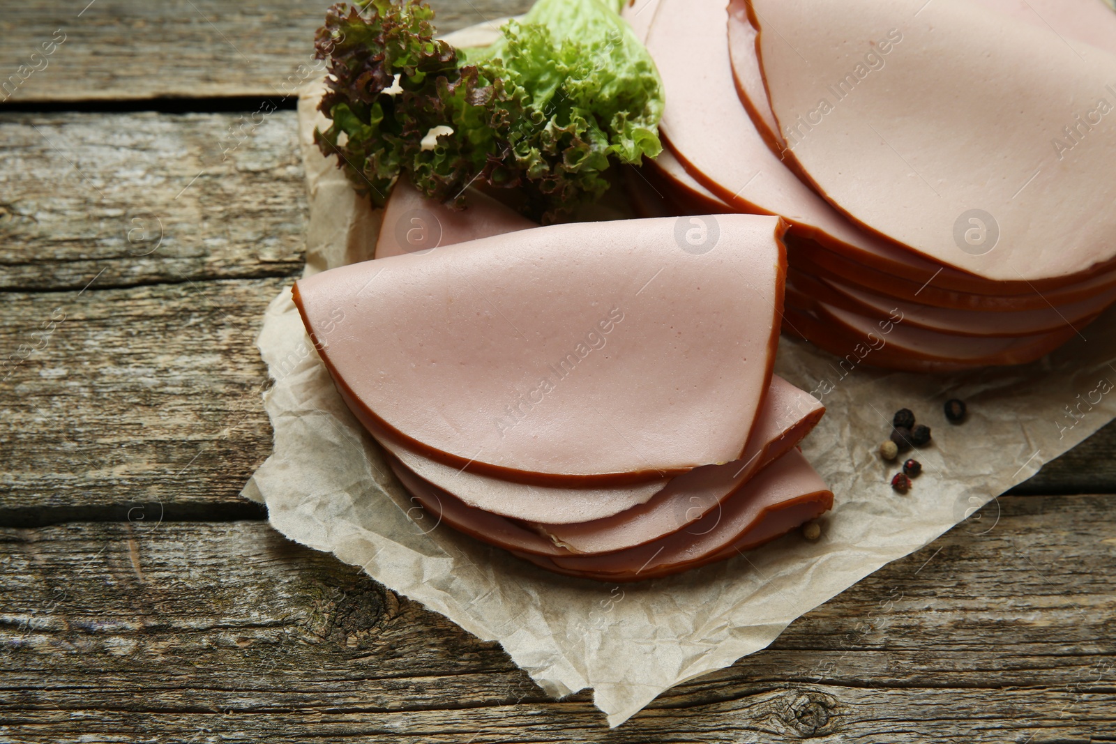 Photo of Slices of delicious boiled sausage with lettuce and spices on wooden table, above view