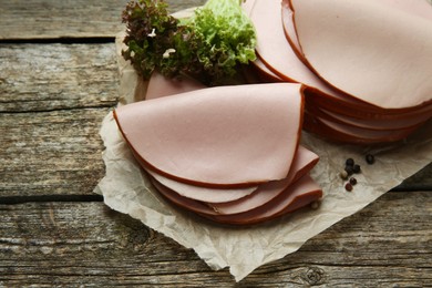 Photo of Slices of delicious boiled sausage with lettuce and spices on wooden table, above view