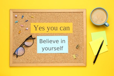 Photo of Corkboard with motivational quotes, cup of coffee and office stationery on yellow background, flat lay