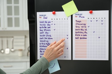 Photo of Woman checking to do list on fridge in kitchen, closeup