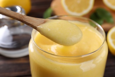 Photo of Taking delicious lemon curd from glass jar at table, closeup