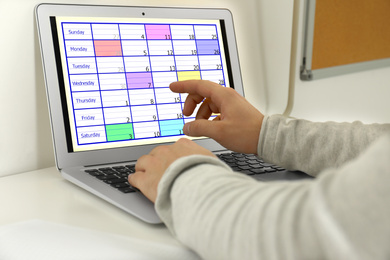 Young man using calendar app on laptop in office, closeup