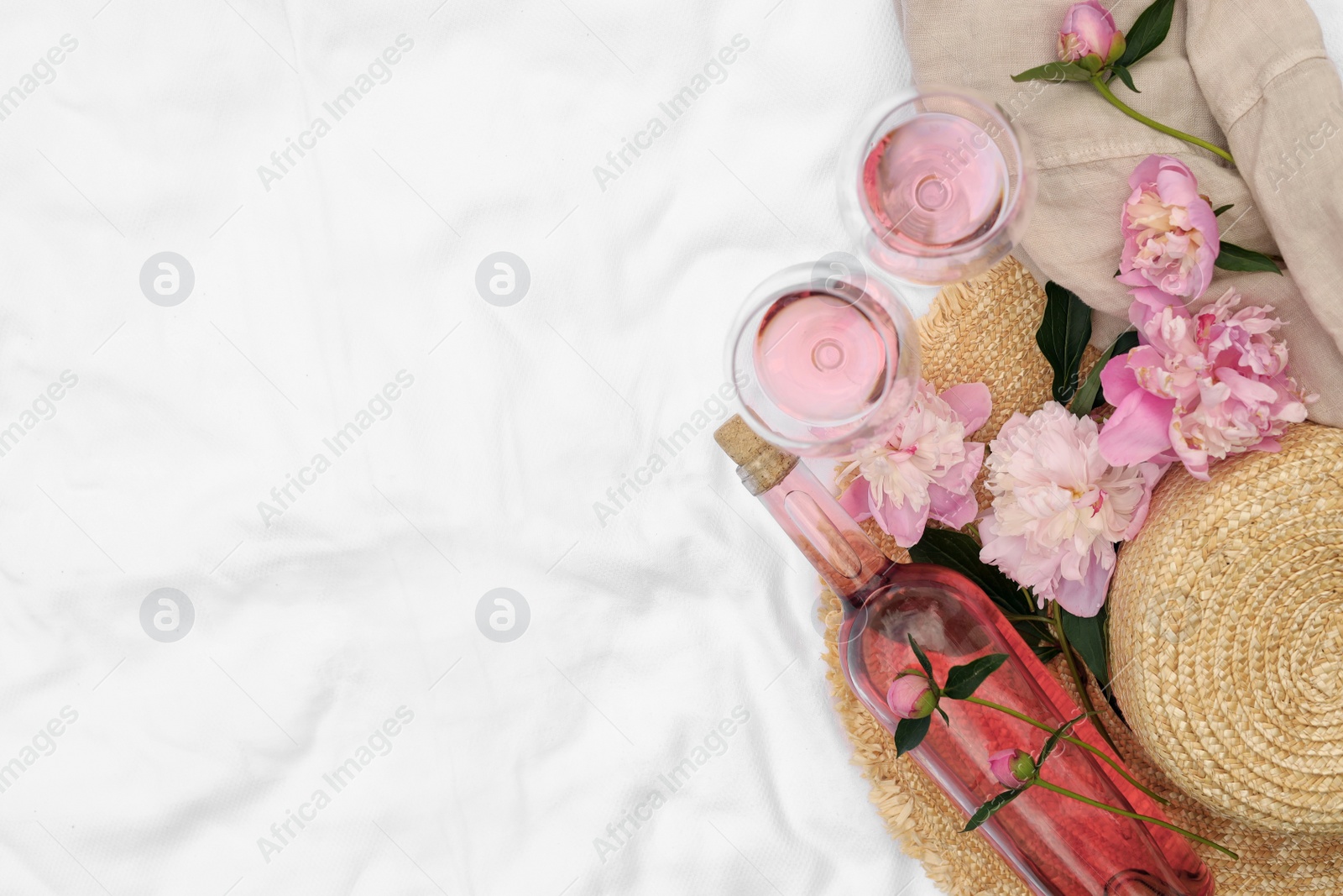 Photo of Flat lay composition with beautiful peonies and rose wine on white fabric, space for text