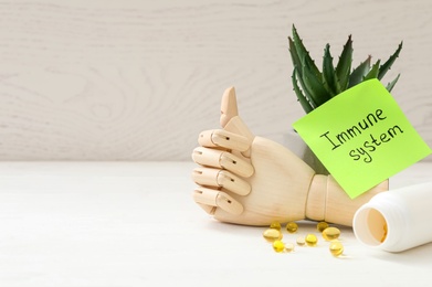 Photo of Mannequin hand, pills and note with phrase Immune System on white wooden table. Space for text