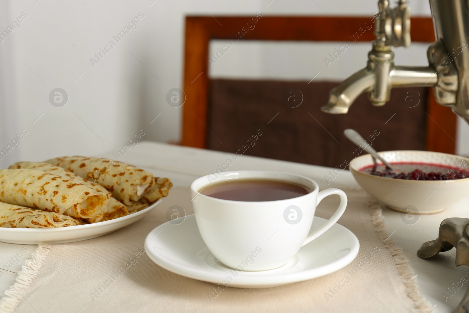 Photo of Vintage samovar, cup of hot drink and snacks served on white wooden table. Traditional Russian tea ceremony