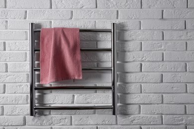 Photo of Modern heated towel rail with warm soft towel on white brick wall. Space for text