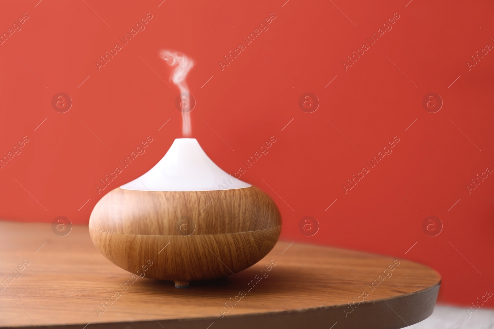 Photo of Essential oils diffuser on wooden table near red wall. Space for text