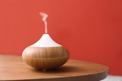 Photo of Essential oils diffuser on wooden table near red wall. Space for text