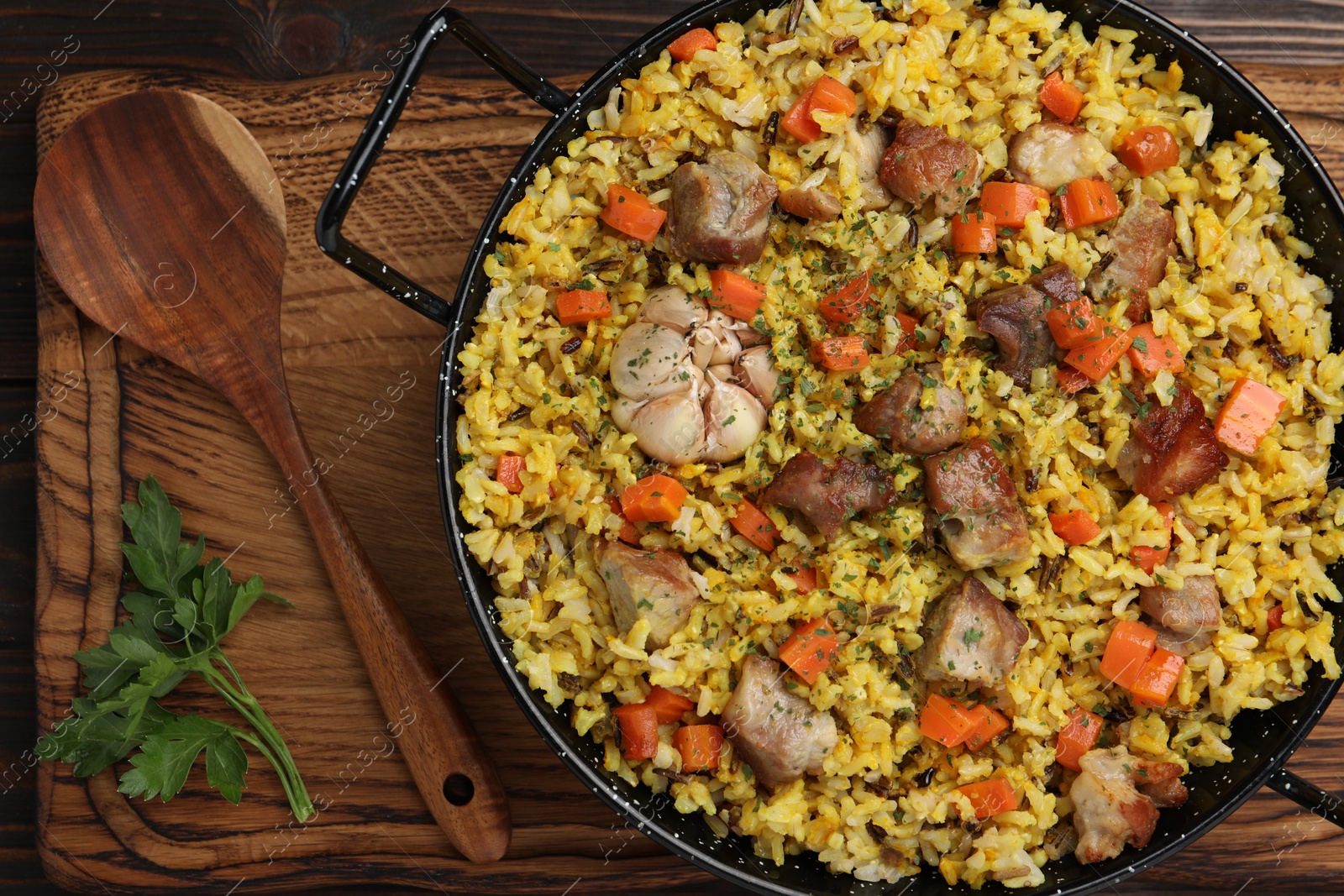 Photo of Delicious pilaf with meat, carrot and garlic served on wooden table, top view