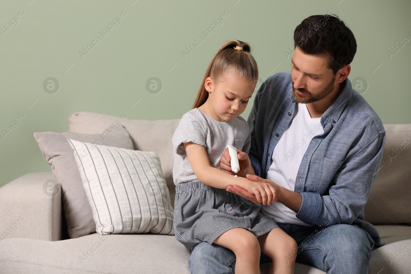 Photo of Father applying ointment onto his daughter's arm on couch