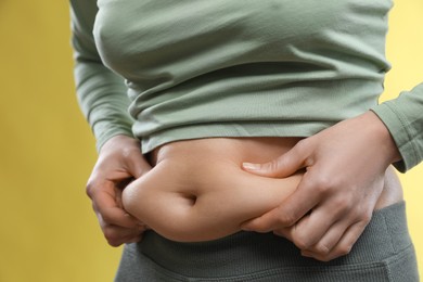 Photo of Woman touching belly fat on yellow background, closeup. Overweight problem