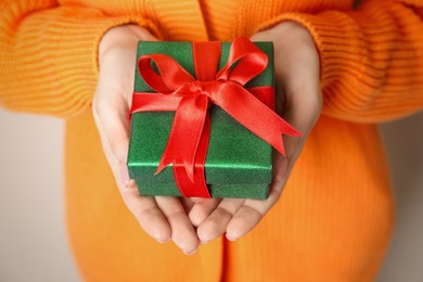 Christmas present. Woman holding beautifully wrapped gift box on beige background, closeup