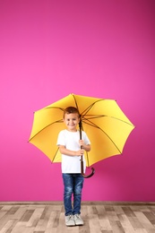 Photo of Little boy with yellow umbrella near color wall