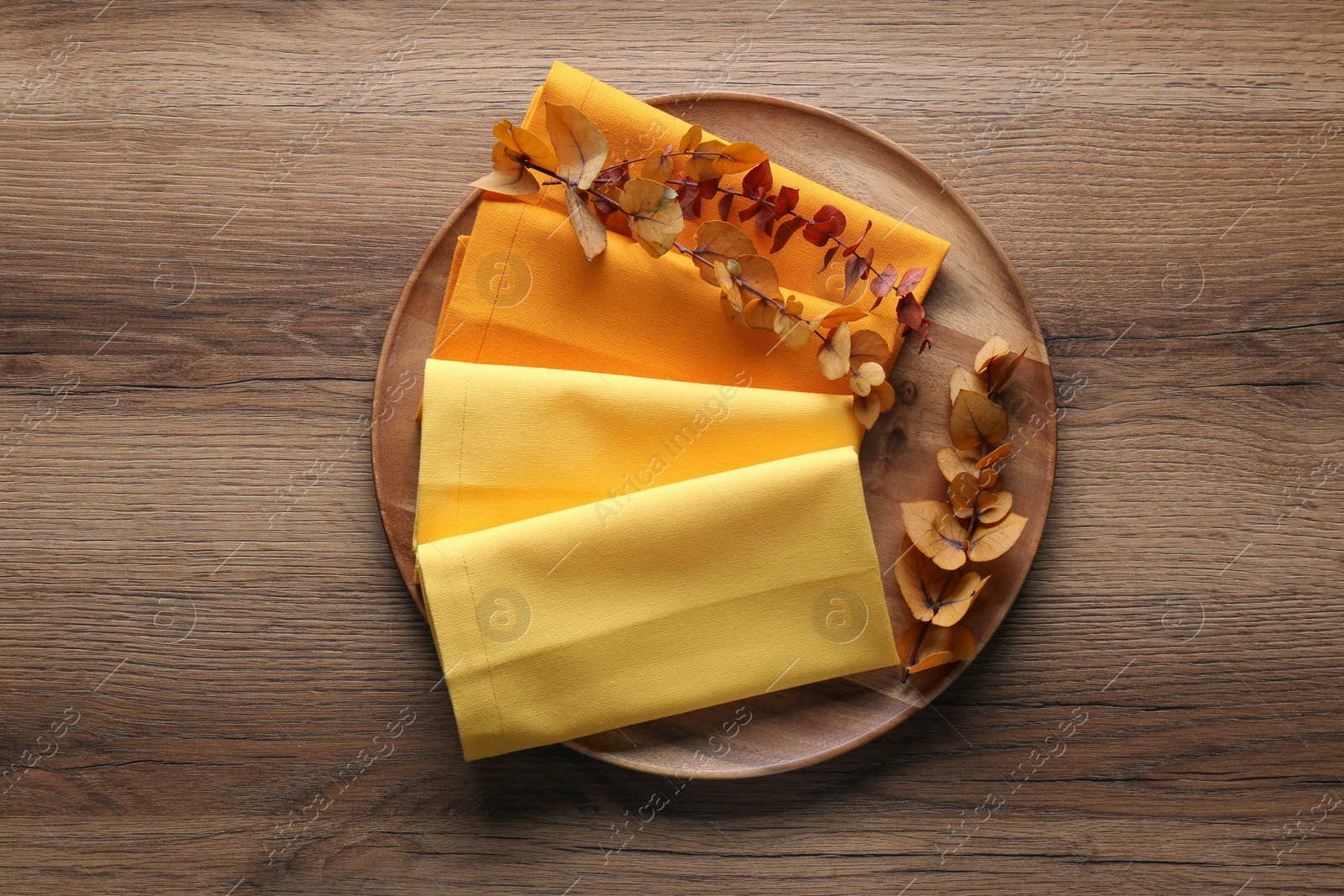 Photo of Tray with different kitchen napkins and decorative dry leaves on wooden table, top view