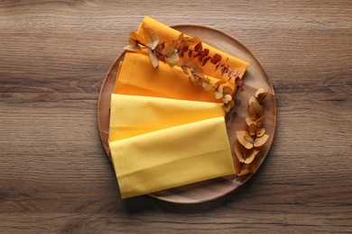 Tray with different kitchen napkins and decorative dry leaves on wooden table, top view