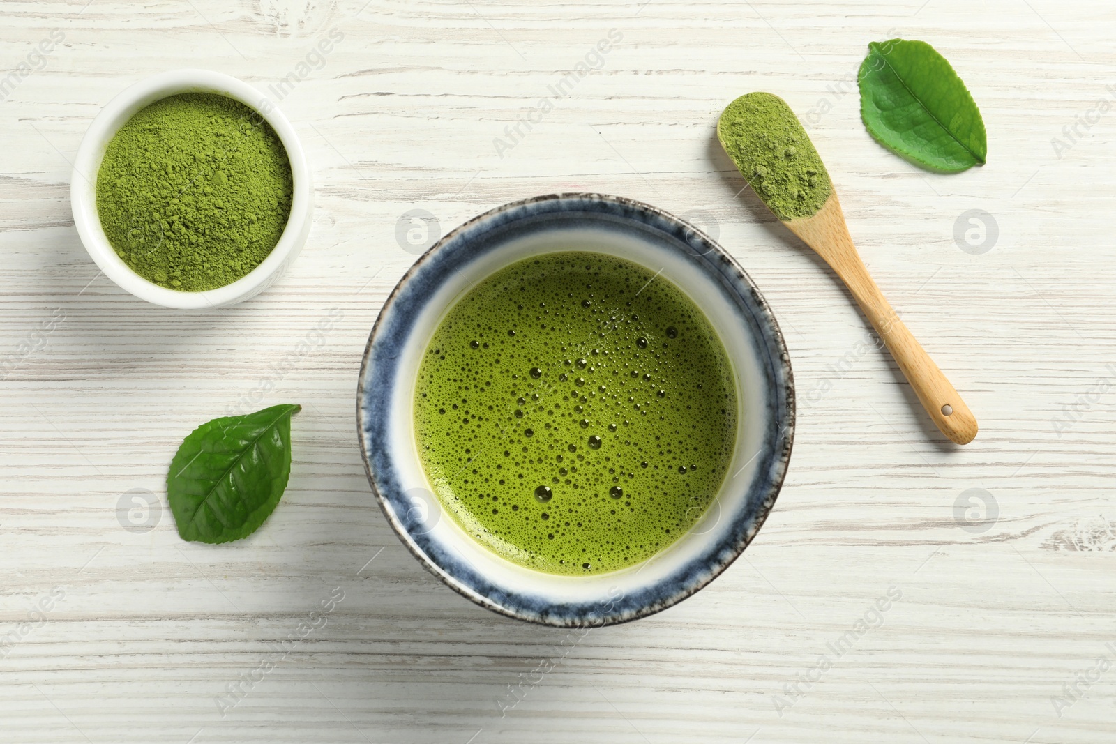 Photo of Cup of fresh matcha tea, green powder and leaves on white wooden table, flat lay