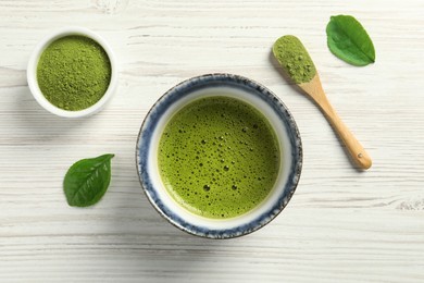 Cup of fresh matcha tea, green powder and leaves on white wooden table, flat lay